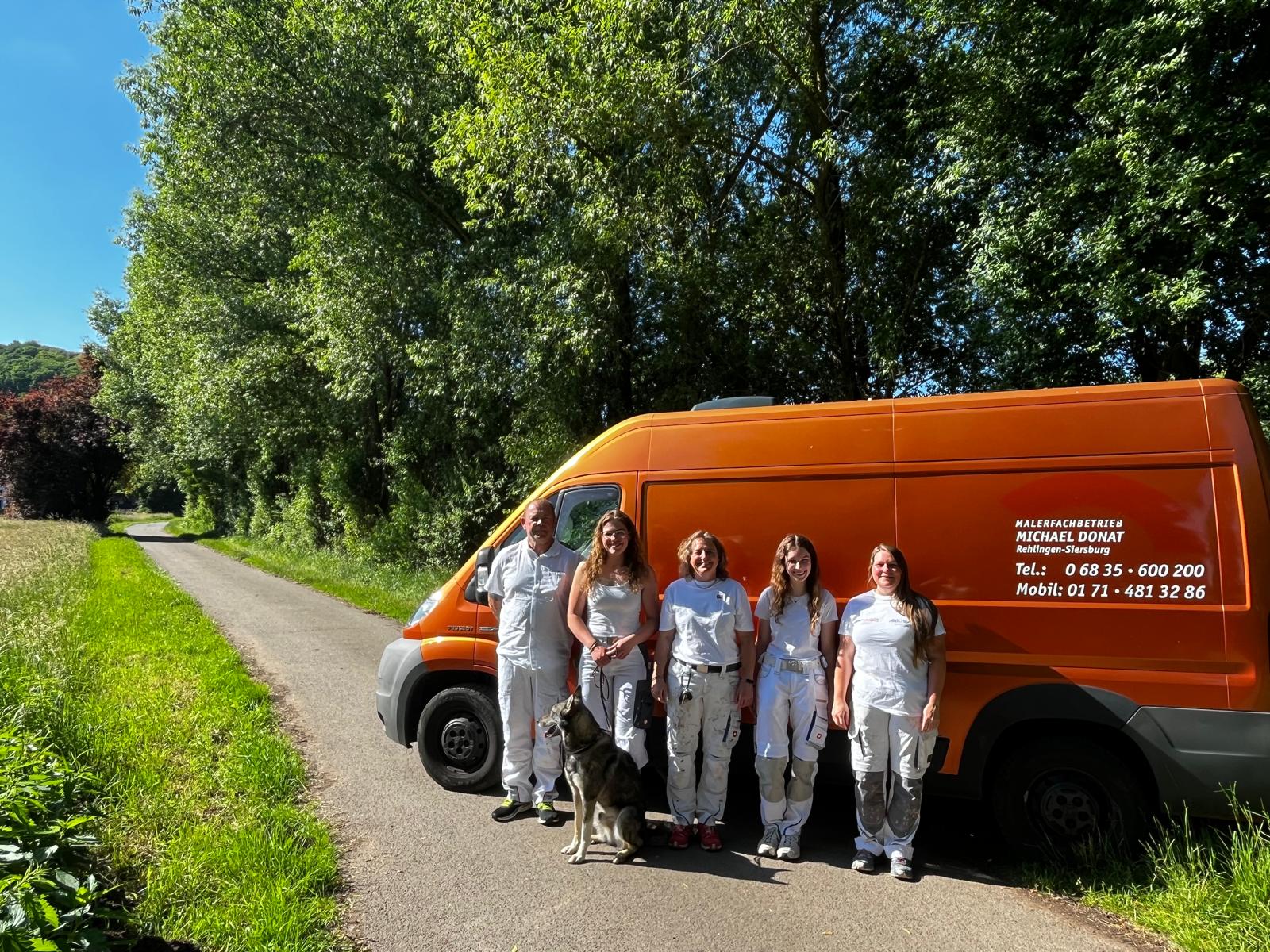 Das Team von Maler-Lacky in weißer Arbeitskleidung vor dem orangen Firmenbus an einem Sommertag